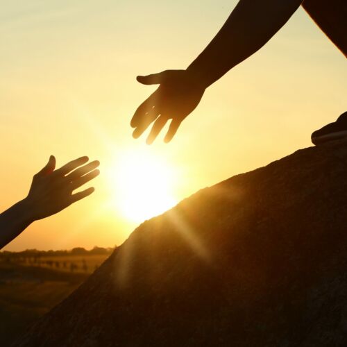 Zwei Personen reichen sich die Hände bei einem Sonnenuntergang